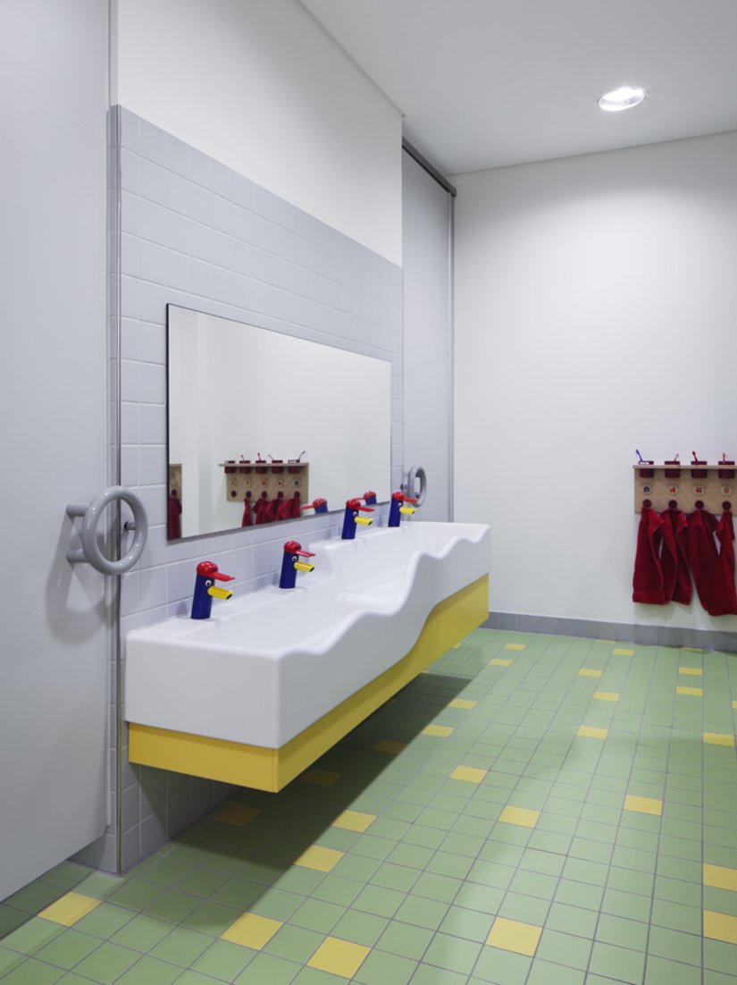 Zachte kleuren in het sanitair, tegels met vrolijke en kleurrijke mozaïeken en gekleurde keramiek stimuleren de kinderen om hun handen te wassen.