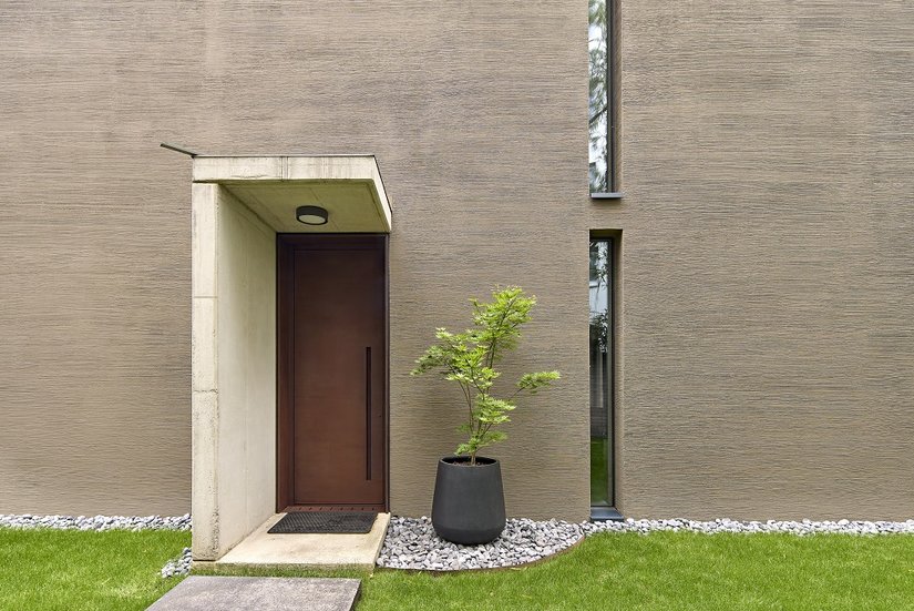 De donkere houten ramen ogen qua vormgeving zeer ingetogen, terwijl de massieve huisdeur van Cortenstaal een duidelijk statement maakt