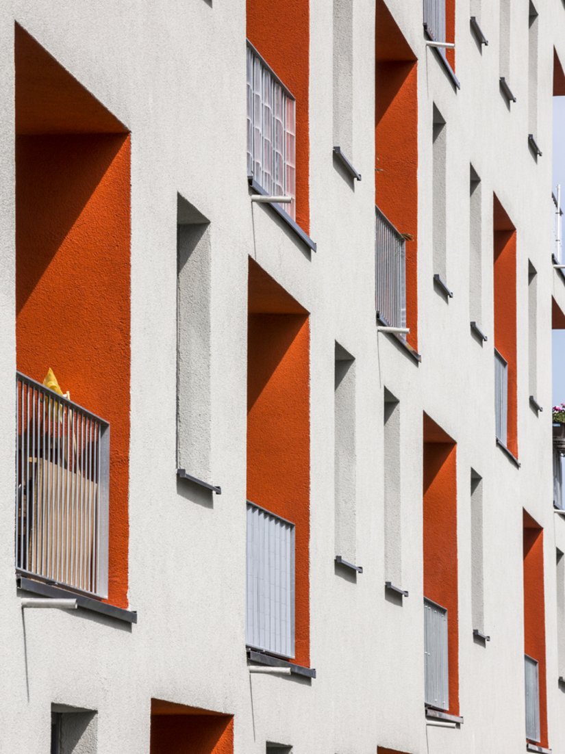 De lichtgrijze gevel wordt onderbroken door opvallende oranjerode loggia’s.