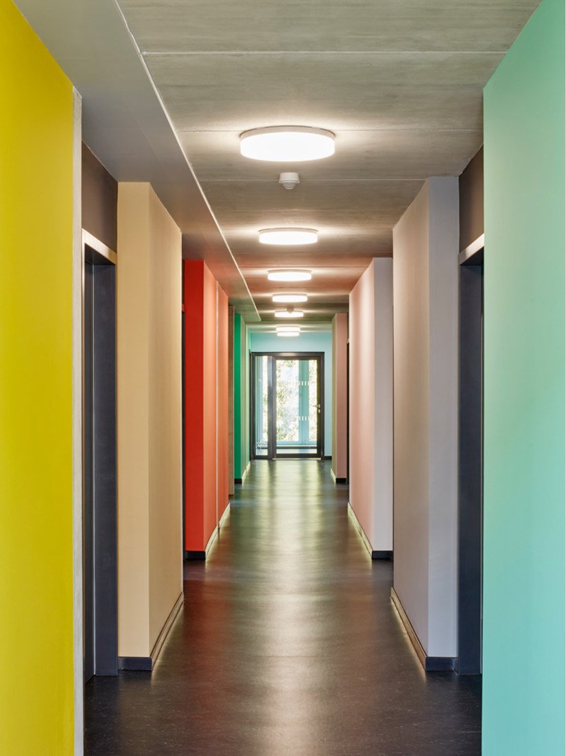 De paden worden begeleid door gekleurde ruiten, die de blik naar de groene buitenruimte leiden of schijnbaar een stapje opzij doen om toegang te geven tot de woonruimten.
Foto © Sigurd Steinprinz / ACMS Archirtekten GmbH