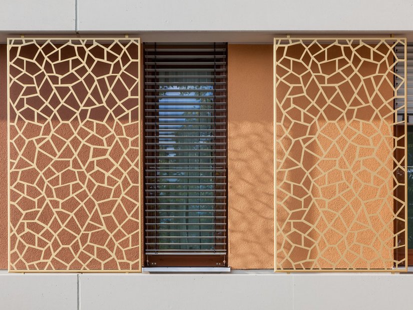 De prachtige ritmering van de gevel met de afwisseling van betonkleurige horizontale banden en verticaal ingesprongen kleurvlakken wordt op speelse wijze aangevuld door de ornamentele elementen.